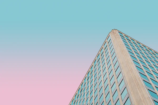 The upper corner of a building somewhere in London, UK. The building's facade is tan, possibly concrete or stone. Each wall has a grid of square shaped, bluish-green windows. Since this photo appears to have been shot at sunset, the sky ranges from blue at its top to a rosy orange below.