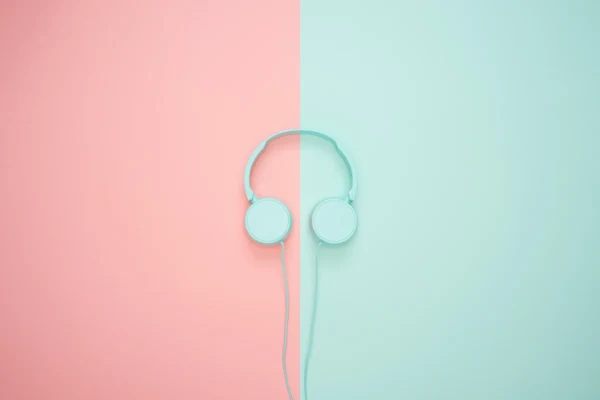 Mint green over-the-ear headphones rest against a color-blocked background. The left half of the background is a rosy pink. The right half is the same mint green as the headphones.